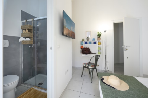 Modern hotel room at Dimore Salentine, Lecce with ensuite bathroom, work desk, shelving, TV, and green accent decor