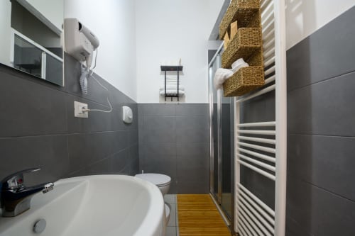 Modern bathroom in Dimore Salentine, Lecce with dark tiles, white toilet, heated towel rail, and wooden floor