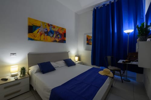 Modern bedroom in Lecce hotel with blue accents, white bedding, city view curtains, and contemporary decor.
