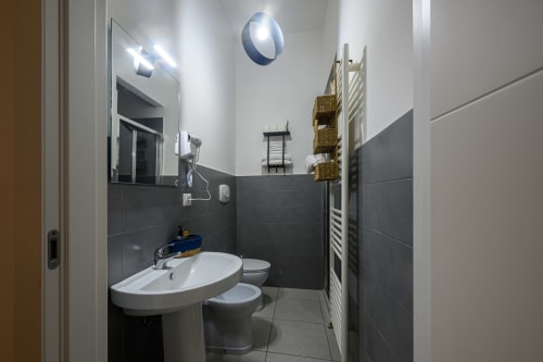 Modern bathroom with dark tile walls, white sink, toilet, and mirror at Dimore Salentine hotel in Lecce
