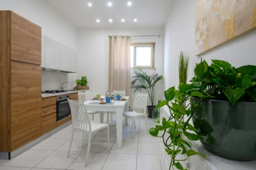 Modern kitchen-dining area at Dimore Salentine in Lecce with white table, wooden cabinetry, and potted plants