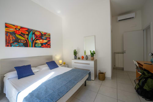 Bright bedroom at Dimore Salentine in Lecce with bed, colorful artwork, dresser with plants, and modern amenities