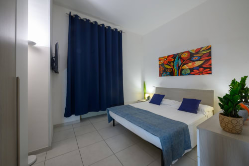 Modern hotel room at Dimore Salentine in Lecce with queen bed, blue accents, TV, and equipped kitchenette
