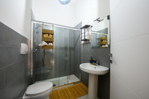 Modern bathroom in Dimore Salentine, Lecce with black tile walls, glass shower enclosure, pedestal sink, and wooden floor
