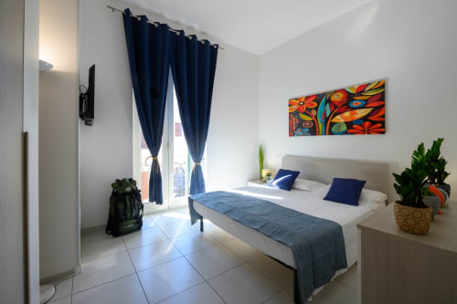 Modern hotel room at Dimore Salentine in Lecce with queen bed, blue curtains, colorful artwork, and city view balcony