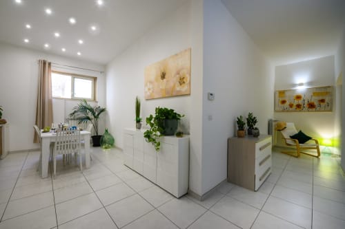 Modern hotel room at Dimore Salentine in Lecce with white furniture, potted plants, artwork, and city view from window