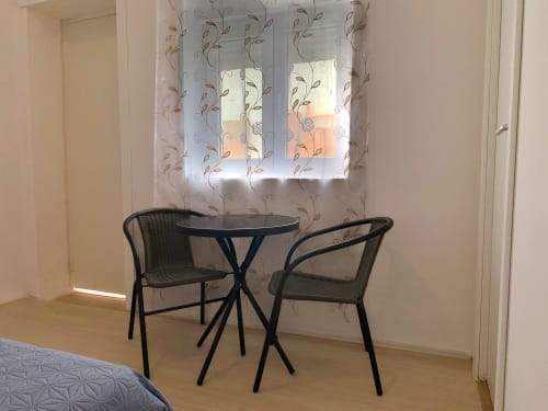 Pequena área de estar no quarto da pousada Anchor House Albufeira com mesa redonda e duas cadeiras de vime perto da janela