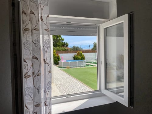 Janela aberta na Anchor House Albufeira com vista para o pátio, piscina e gramado verde