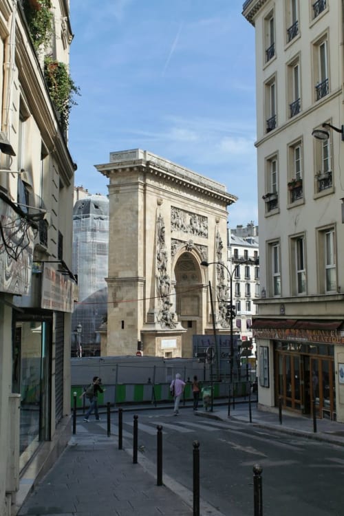 Arche en pierre historique dans une rue parisienne avec immeubles classiques et gratte-ciel modernes en arrière-plan