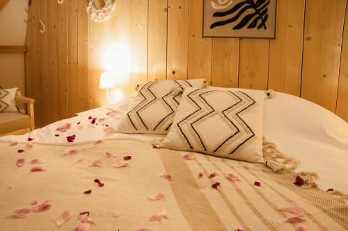 Chambre romantique aux Cabanes du Nideck avec murs en bois, coussins décorés et pétales de rose à Oberhaslach