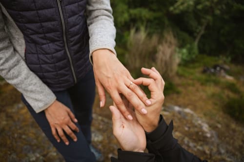 Mains du couple empilées ensemble aux Cabanes du Nideck à Oberhaslach, montrant la bague de fiançailles et un moment de complicité
