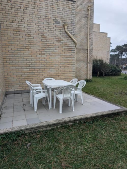Mobiliário de jantar branco ao ar livre no pátio da Villas Eden, apartamento rural em Fão, Portugal, com vista para edifício de tijolos e jardim