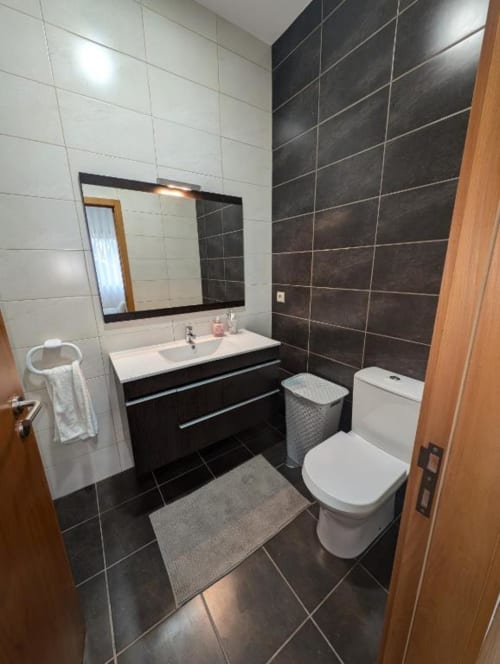 Banheiro moderno em Villas Eden com azulejos pretos, pia branca, vaso sanitário e toalheiro aquecido