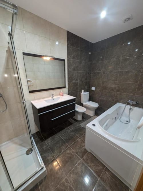 Banheiro moderno em Villas Eden com paredes de azulejo escuro, gabinete branco com espelho, banheira, vaso sanitário, bidê e chuveiro tipo walk-in