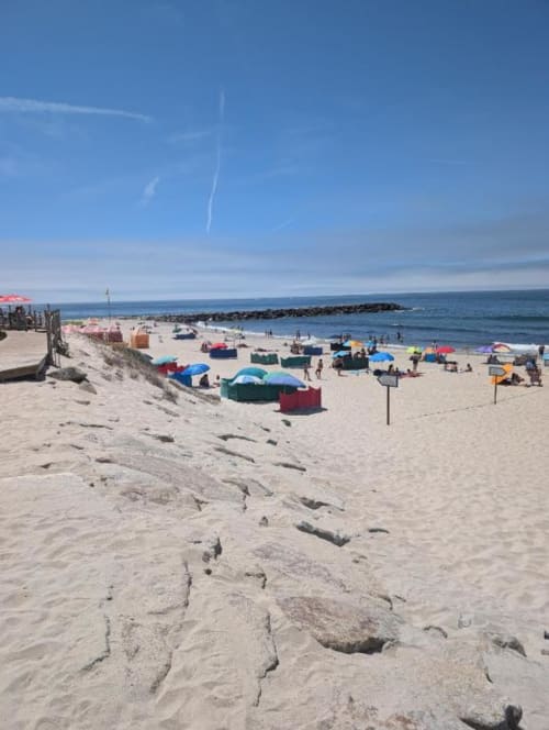 Praia movimentada de Fão com guarda-sóis coloridos, areia, oceano e quebra-mar rochoso em dia claro