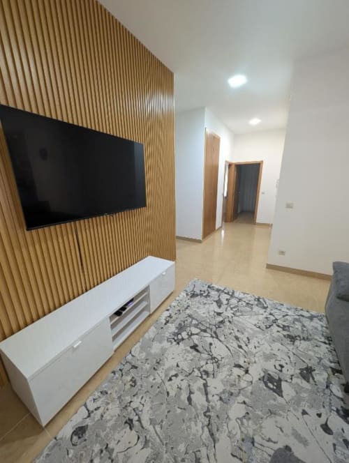 Sala de estar moderna em Villas Eden com TV de tela plana, rack branco, tapete estampado e parede de madeira