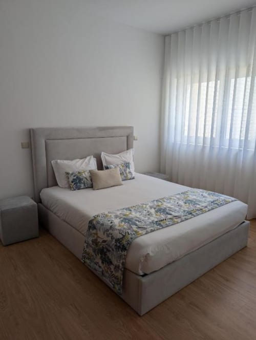 Quarto moderno com cama estofada em bege, roupa de cama branca e tapete floral nas Villas Eden em Fão, Portugal