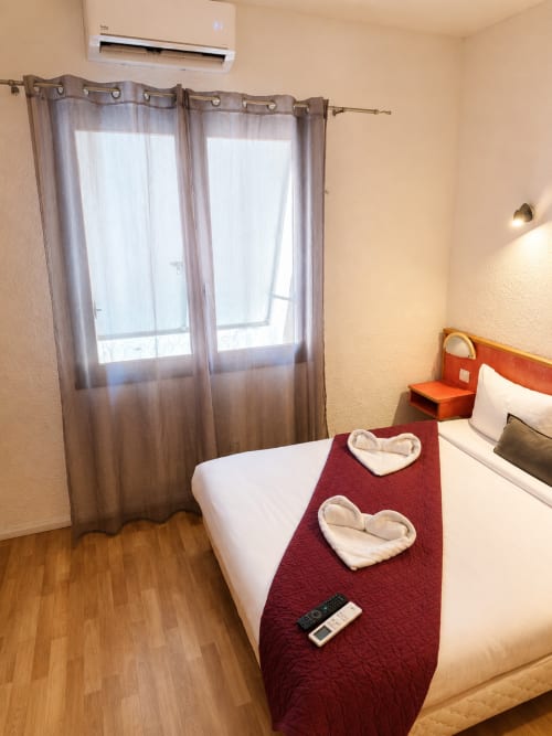 Chambre moderne de l'Hôtel Les Alizés avec lit double, serviettes en forme de cœur et vue montagne par portes-fenêtres