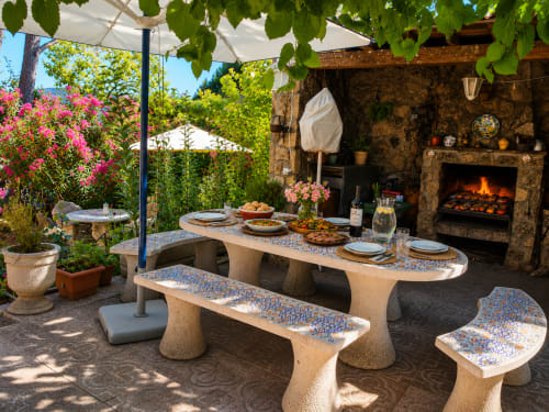 Rústico comedor al aire libre en Las Casitas de Noe, Pelayos de La presa: mesa de piedra, barbacoa, plantas floridas y jardin en sombra