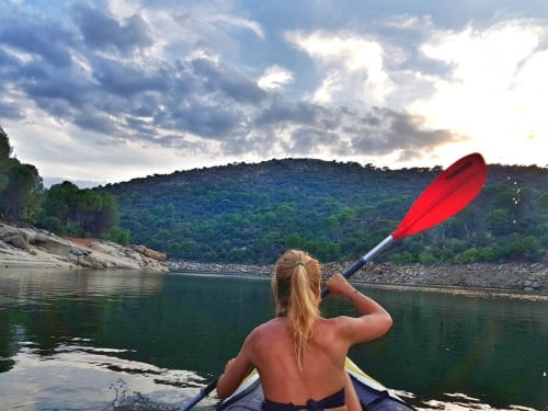 Mujer en kayak en el Pantano de San Juan junto a montañas  boscosas de pinos en Las Casitas de Noe, San martin de Valdeiglesias España