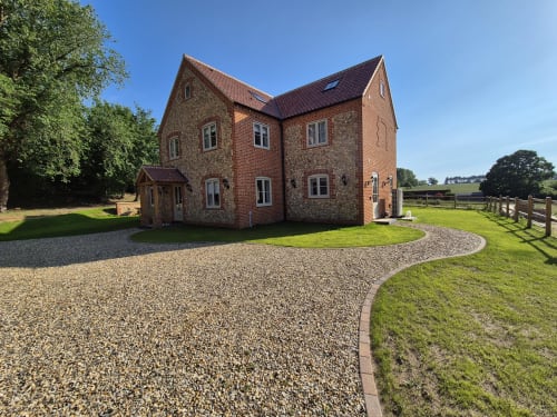Brick and stone cottage in Fakenham with gravel driveway, manicured garden, and countryside views
