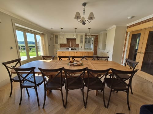 Spacious dining room at Rose Vill Homes cottage with large wooden table, black chairs, and garden views through patio doors.