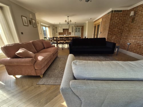 Spacious living room with brown and gray sofas, dining area, and brick kitchen in Willy Mansion cottage at Rose Vill Homes,