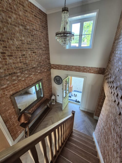 Elegant stairwell at Rose Vill Homes cottage in Fakenham with exposed brick walls, crystal chandelier, and wooden railings
