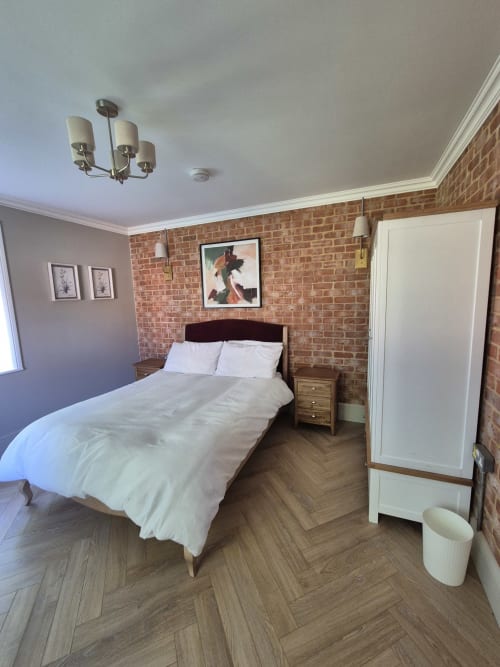 Modern bedroom at Rose Vill Homes cottage in Fakenham with brick accent wall, queen bed, hardwood floors, and white wardrobe.