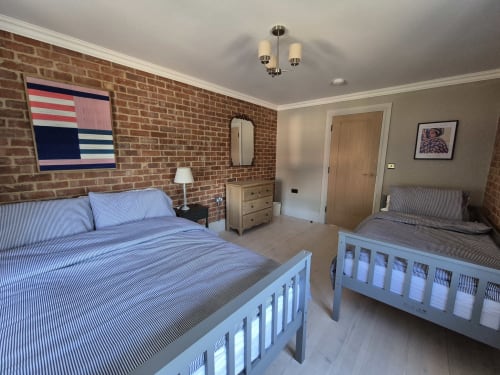 Spacious cottage bedroom at Rose Vill Homes, Fakenham with two single beds, exposed brick wall, and modern furnishings
