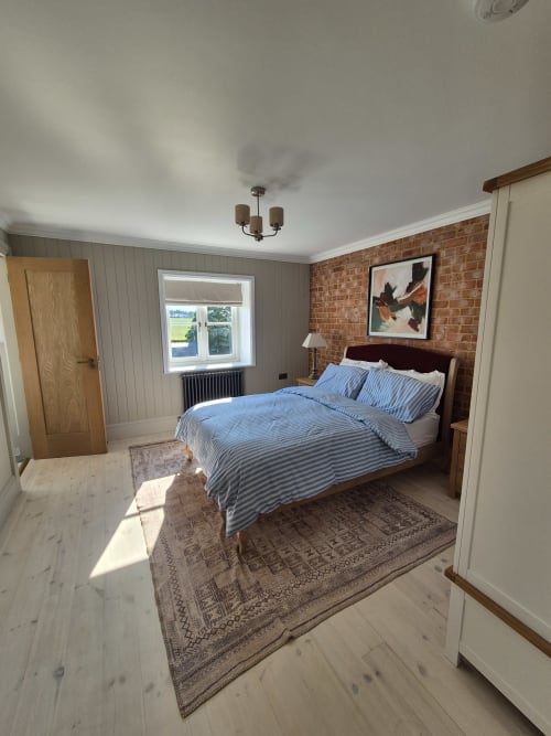 Bright bedroom in Rose Vill Homes cottage, Fakenham, with blue striped bedding, brick accent wall, wooden bed frame, and