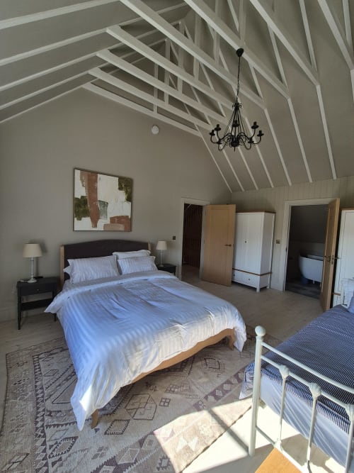 Spacious bedroom in Rose Vill Homes cottage with vaulted ceilings, queen bed, chandelier, and garden view in Fakenham