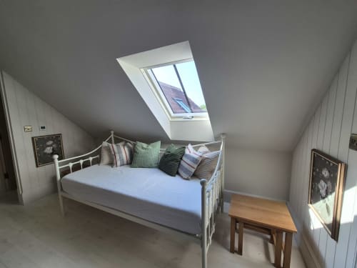 Cozy attic bedroom in Rose Vill Homes cottage with skylight, white metal bed, decorative pillows, wooden desk, and hardwood