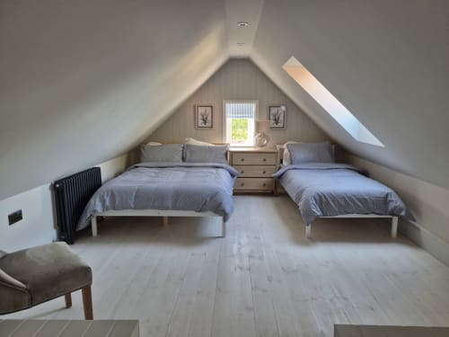 Bright attic bedroom at Rose Vill Homes cottage in Fakenham with two beds, wooden floors, and garden view through skylights
