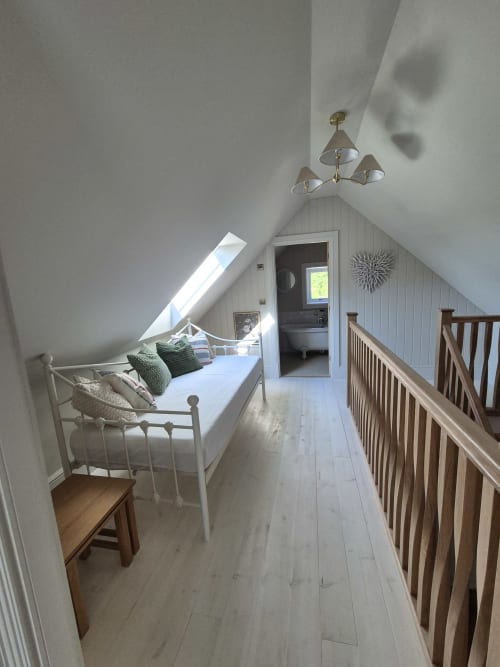 Bright attic bedroom at Rose Vill Homes cottage with white metal bed, wooden railings, skylights, and ensuite access in