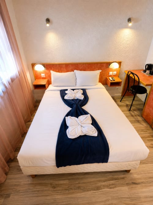 Chambre double à l'Hôtel Les Alizés, Le Pouzin, avec literie blanche, serviettes décoratives, tête de lit en bois et éclairage ambiant