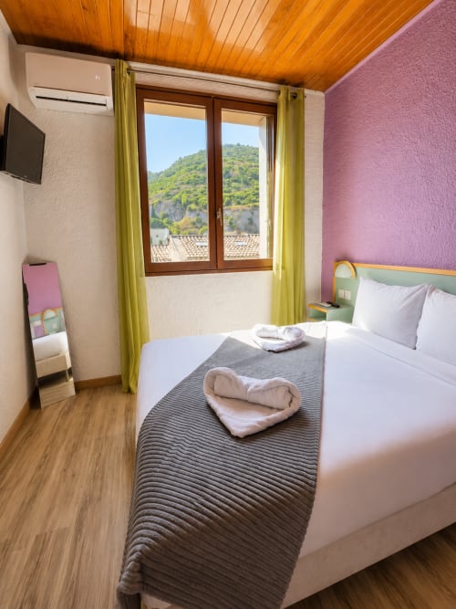 Chambre double cosy à l'Hôtel Les Alizés avec vue montagne, plafond en bois, mur d'accent rose et serviette en cœur sur le lit
