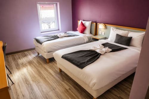 Chambre triple de l'Hôtel Les Alizés avec deux lits, murs violets, parquet et vue sur le jardin
