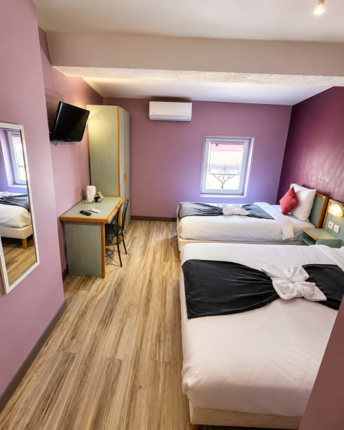Chambre triple de l'Hôtel Les Alizés aux murs roses, deux lits, bureau, TV et parquet à Le Pouzin