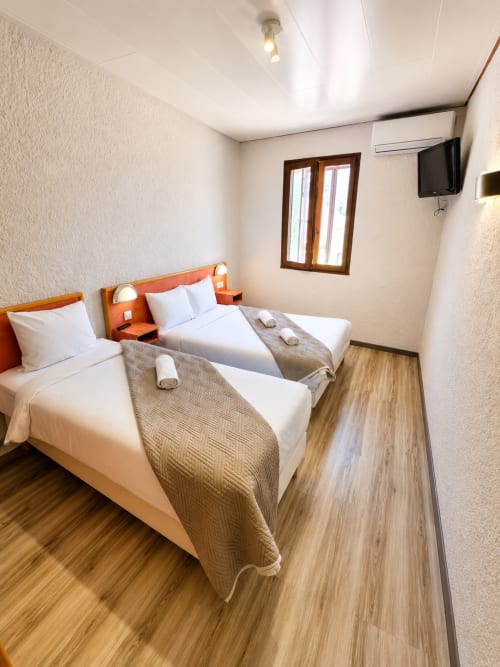 Chambre triple à l'Hôtel Les Alizés avec deux lits, têtes de lit orange, télévision et parquet à Le Pouzin