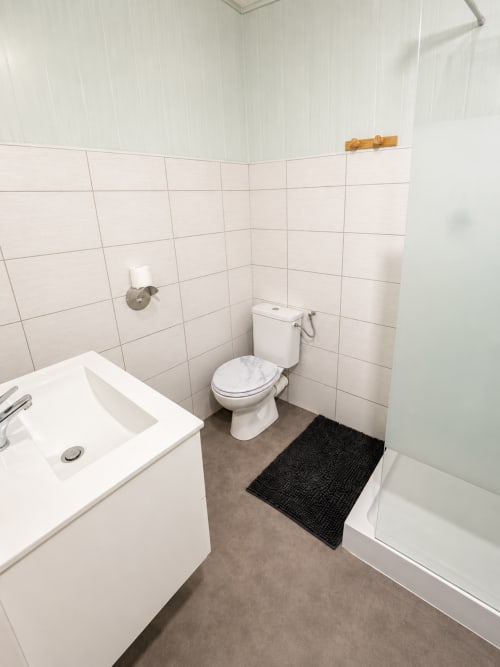 Salle de bains immaculée aux carrelages blancs, toilettes, lavabo et baignoire à l'Hôtel Les Alizés au Pouzin