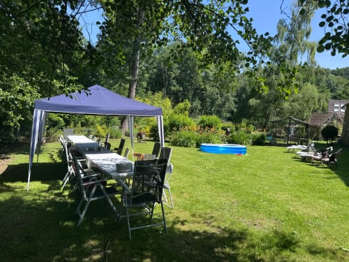 Jardin extérieur du BnB Le Clos du Buisson avec auvent bleu, coin repas, piscine et arbres luxuriants