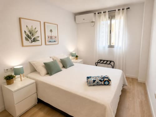 Dormitorio moderno y luminoso con ropa de cama blanca, almohadas verdes, pisos de madera y arte costero en ML Apartments, Picanya