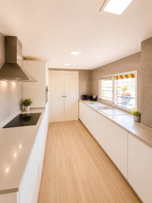 Moderna cocina de galera con muebles blancos, suelo de madera y ventanal con vistas al mar en ML Apartments, Picanya