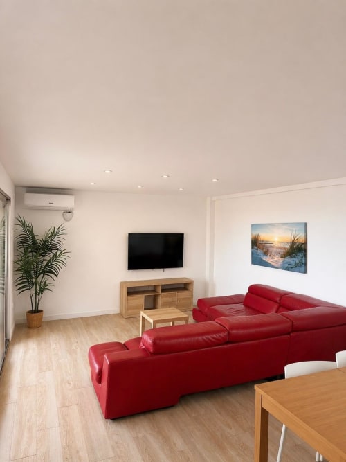 Sala moderna con sofá rojo de cuero, mueble de TV de madera, cuadros de vista marina y piso de madera clara en ML Apartments