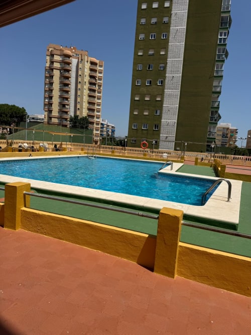 Piscina exterior de ML Apartments en Picanya, España, con agua azul, barreras amarillas y edificios residenciales