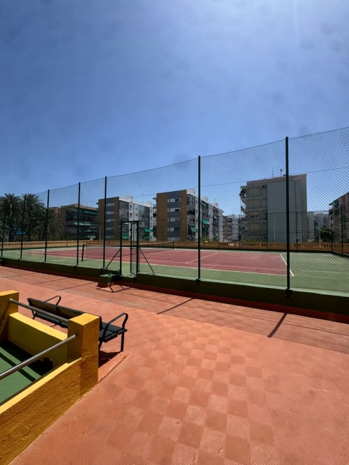 Canchas de tenis al aire libre en ML Apartments en Picanya con edificios residenciales de varios pisos y palmeras bajo cielo azul despejado