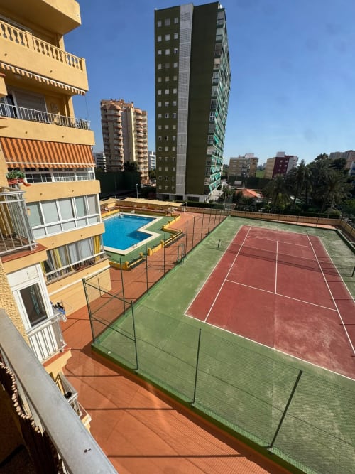 Apartamentos ML Picanya: Pistas de tenis y piscina en complejo residencial con edificios de apartamentos bajo cielo azul despejado