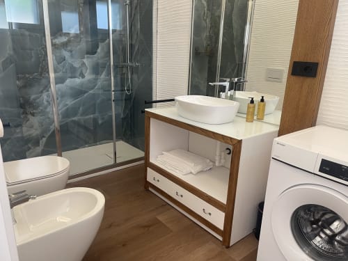Modern bathroom in Palau apartment with white vessel sink, wood vanity, shower enclosure, toilet, and washing machine