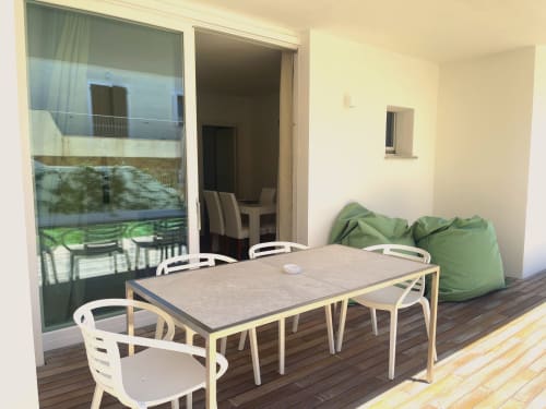 Terrazza dell'appartamento con vista sul giardino a Like at Home Palau, tavolo da pranzo, sedie bianche e pouf verdi